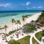 Larga playa casi desierta con palmeras frente al mar turquesa transparente en Zanzíbar Tanzania