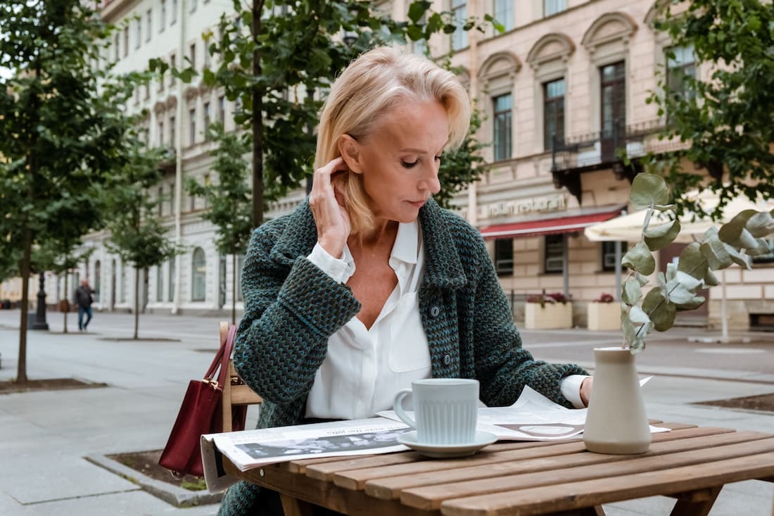 Viajera sola desayunando en terraza de café europeo con libro viajando sola después de los 50