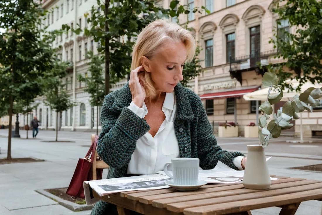 Viajera sola desayunando en terraza de café europeo con libro viajando sola después de los 50