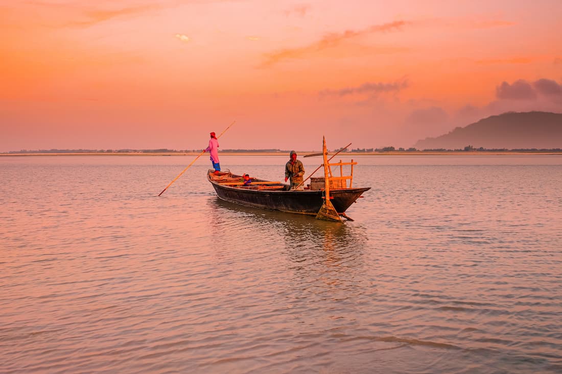 Barca de pescadores en el río Mekong al atardecer con cielo naranja intenso y montañas al fondo en Luang Prabang Laos