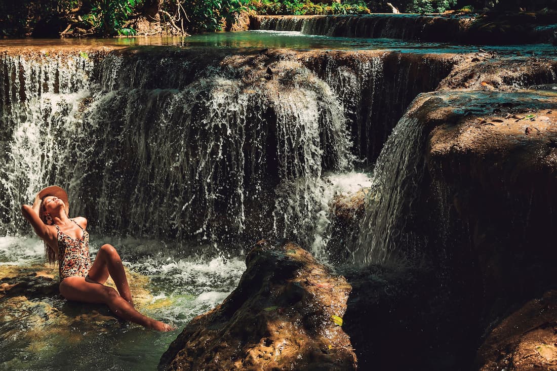 Mujer descansando junto a cascadas escalonadas con pozas de agua esmeralda en Kuang Si cerca de Luang Prabang Laos