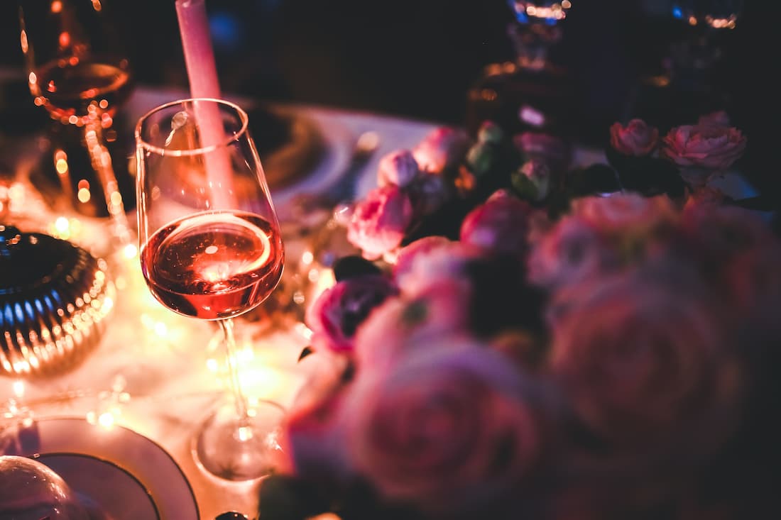 Copa de vino rosado en mesa elegante con velas y flores rosas evocando la cena de gala a bordo del Blue Train Sudáfrica
