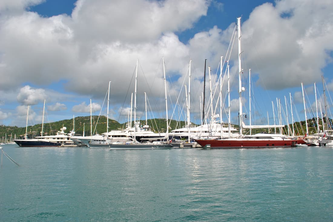 Marina con yates y veleros de lujo anclados en aguas turquesas caribeñas con colinas verdes al fondo en Roatán Honduras