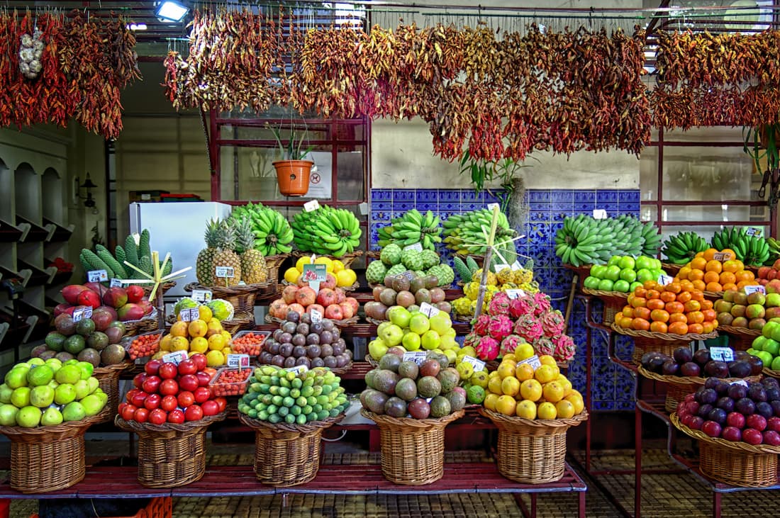 Puesto de frutas tropicales en cestas de mimbre con azulejos azules al fondo en mercado local portugués turismo lento gastronomía auténtica
