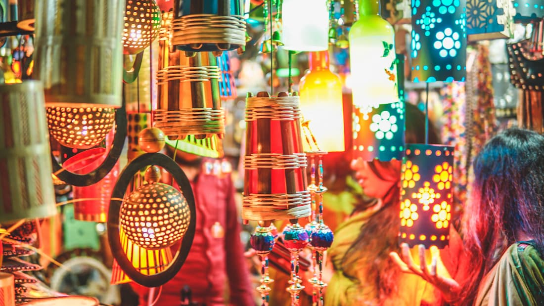 Puesto de faroles y lámparas artesanales de colores en el mercado nocturno de Luang Prabang Laos con visitante admirando los productos