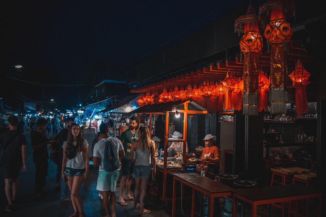 Mercado nocturno de Chiang Mai con faroles rojos tradicionales colgando sobre puestos de comida y turistas paseando Tailandia