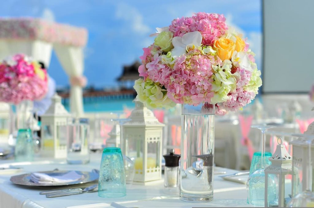 Mesa romántica decorada con flores hortensias rosas y linternas blancas con mar turquesa de Maldivas al fondo luna de miel de lujo