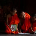 Tres monjes jóvenes con túnicas naranjas estudiando y riendo en el interior de un templo en Luang Prabang Laos