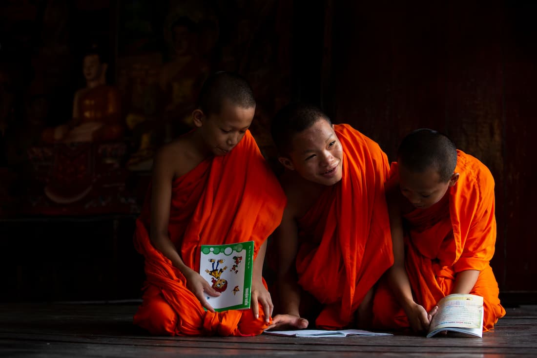 Tres monjes jóvenes con túnicas naranjas estudiando y riendo en el interior de un templo en Luang Prabang Laos