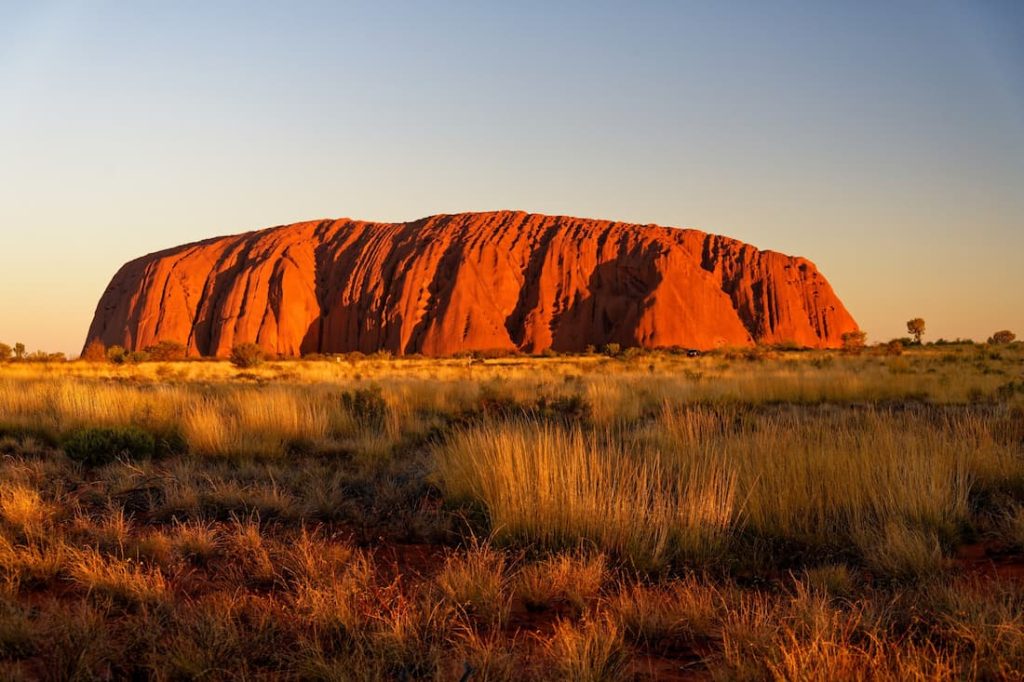 Uluru al atardecer con cielo naranja en el outback australiano parada emblemática del tren The Ghan