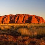 Uluru al atardecer con cielo naranja en el outback australiano parada emblemática del tren The Ghan