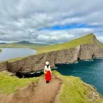 Viajera de espaldas con falda roja contemplando acantilados verdes y lago de las Islas Feroe destinos para el viajero que ya lo ha visto todo