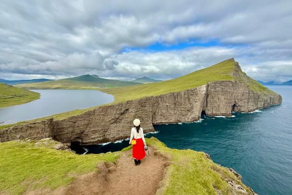 Viajera de espaldas con falda roja contemplando acantilados verdes y lago de las Islas Feroe destinos para el viajero que ya lo ha visto todo