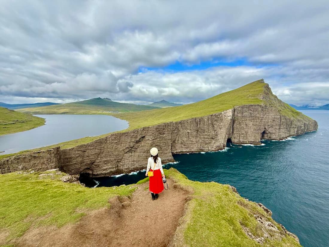 Viajera de espaldas con falda roja contemplando acantilados verdes y lago de las Islas Feroe destinos para el viajero que ya lo ha visto todo
