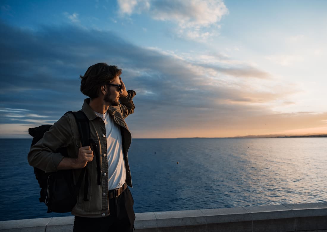 Viajero con gafas de sol mirando el horizonte al atardecer junto al mar evocando la contemplación del paisaje desde el Blue Train Sudáfrica