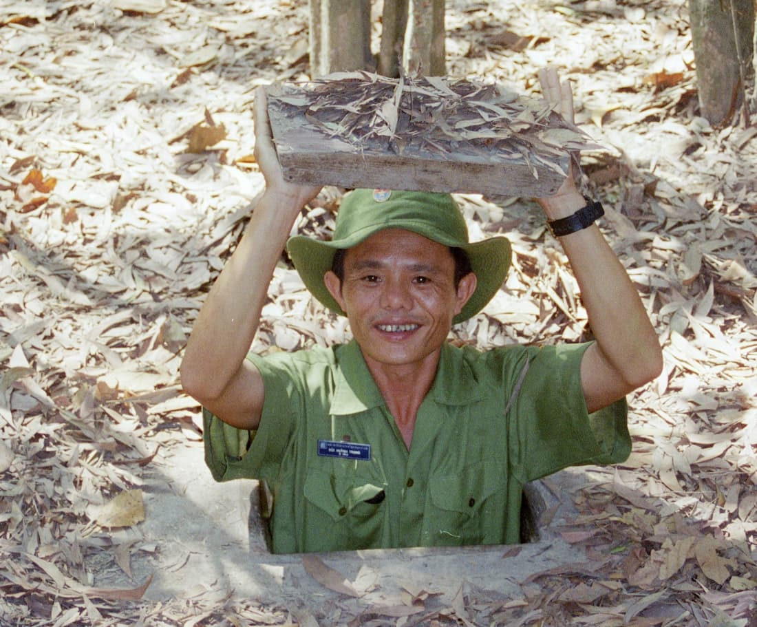 Guía vietnamita emergiendo de la entrada camuflada de los túneles de Cu Chi con trampilla de madera Ho Chi Minh Vietnam