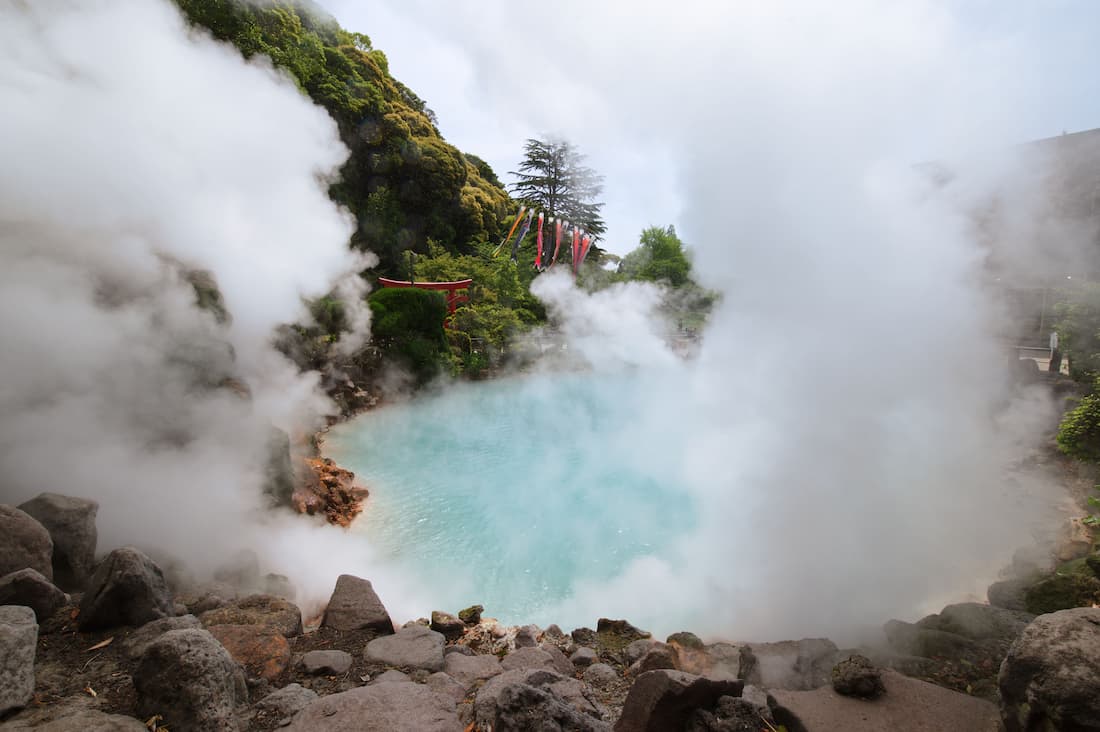 Infierno termal de Beppu con agua turquesa hirviendo y vapor denso rodeado de rocas volcánicas y torii rojo Kyushu Japón