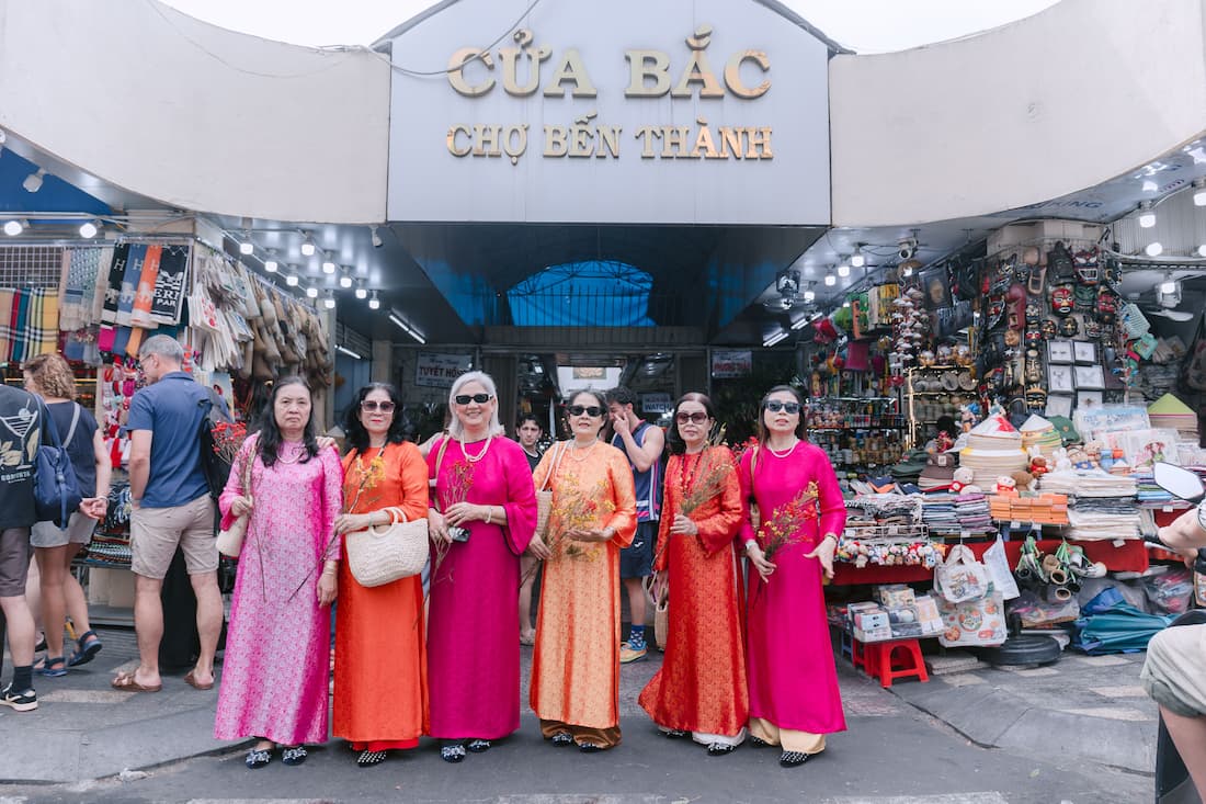 Mujeres vietnamitas con ao dai tradicionales frente a la entrada del mercado Ben Thanh en Ho Chi Minh Vietnam