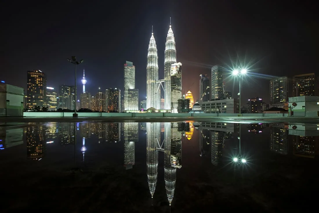Torres Petronas iluminadas de noche reflejadas en el agua con el skyline de Kuala Lumpur Malaysia