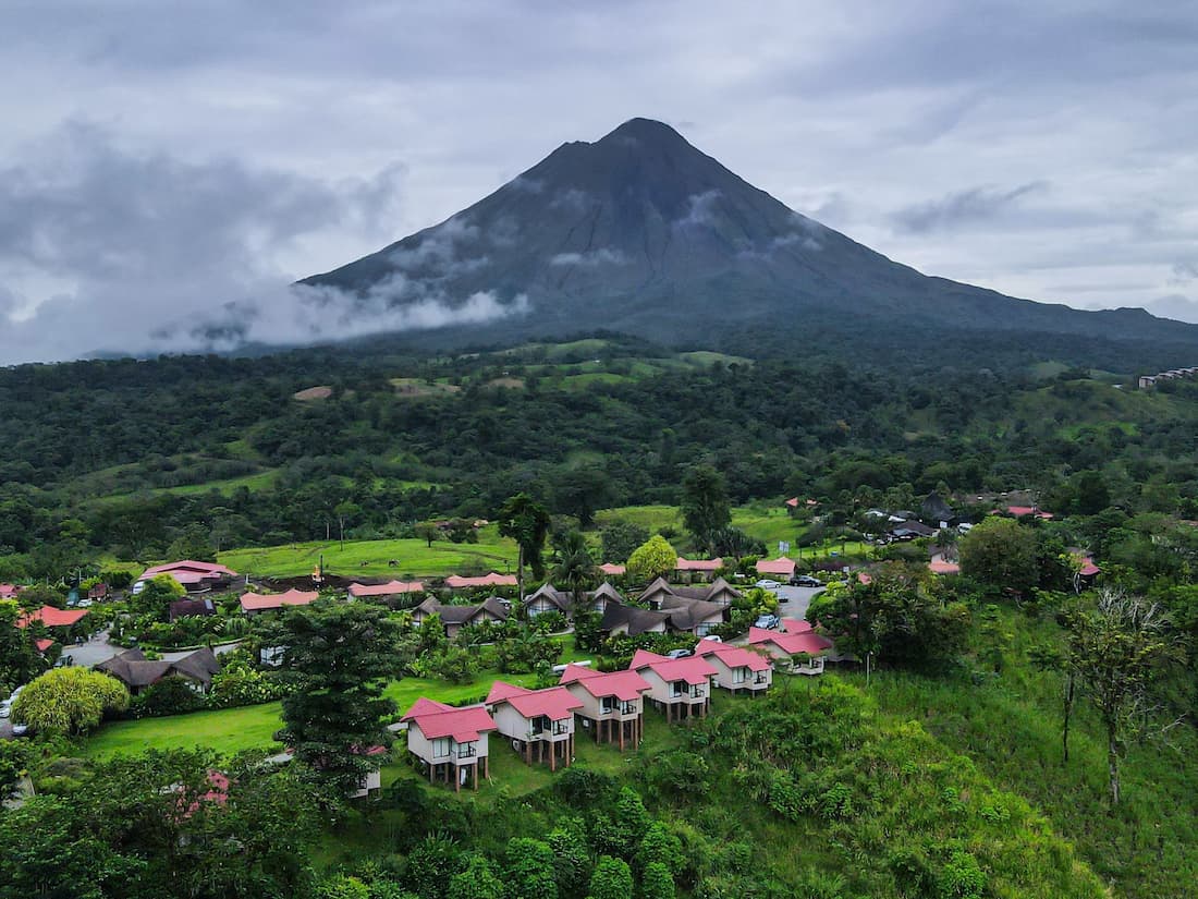 Vista aérea del volcán Arenal con lodges de tejados rojos rodeados de vegetación tropical en Costa Rica ecoturismo